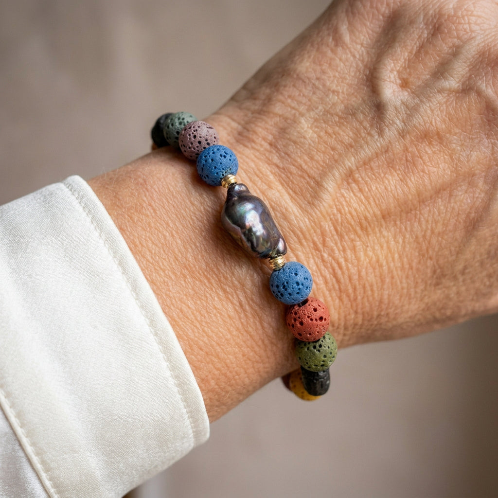 Dark iridescent keshi pearl bracelet with porous blue, pink, green and black lava beads and sterling silver spacers, worn on the wrist beside a white silk shirt cuff.