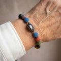 Dark iridescent keshi pearl bracelet with porous blue, pink, green and black lava beads and sterling silver spacers, worn on the wrist beside a white silk shirt cuff.