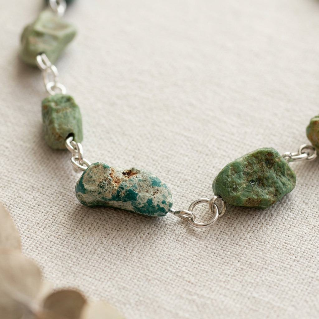 Close-up of two raw Hubei turquoise stones joined by a round sterling silver connecting ring, showing rough green-blue surfaces with cream and brown matrix on pale satin.
