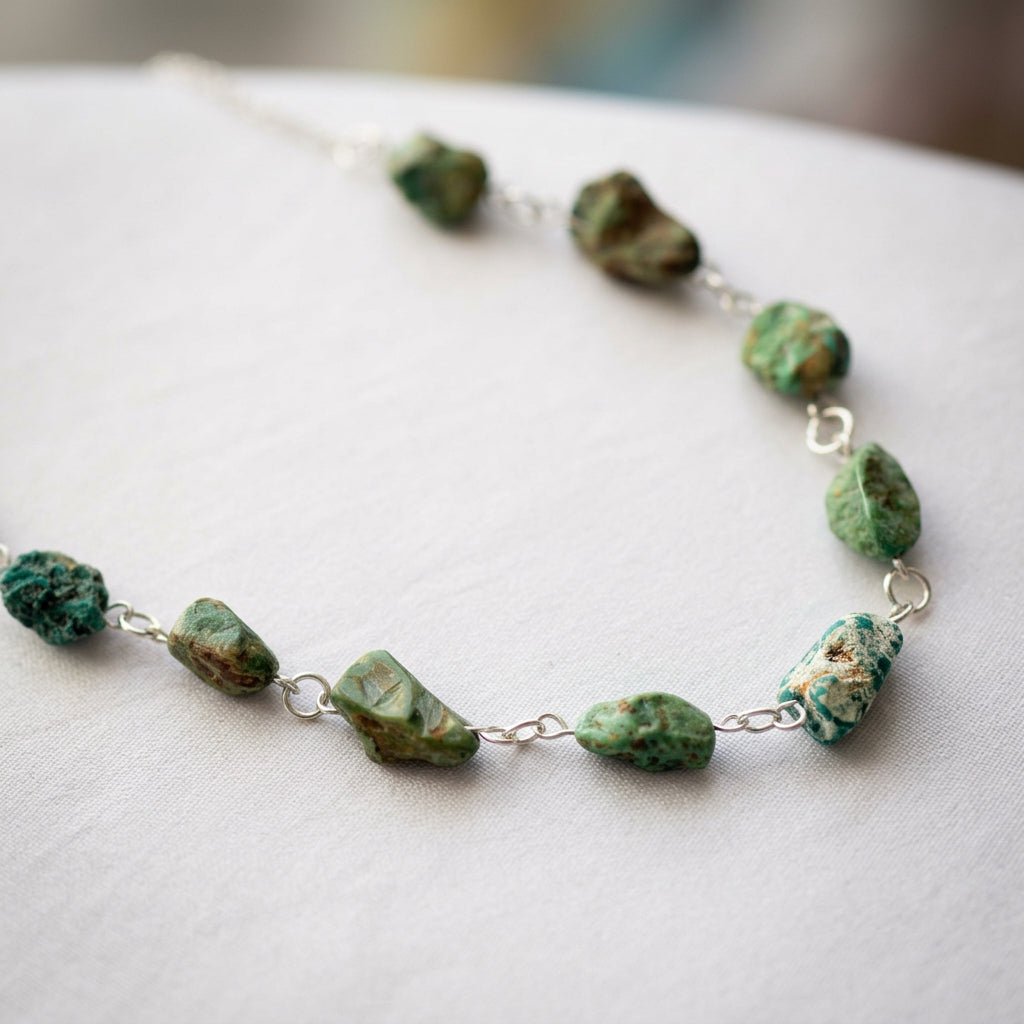 Raw Hubei turquoise necklace arranged in a wide curve on cream satin, showing uneven green-blue stones with brown and pale matrix patterns, joined by handmade sterling silver wire links.