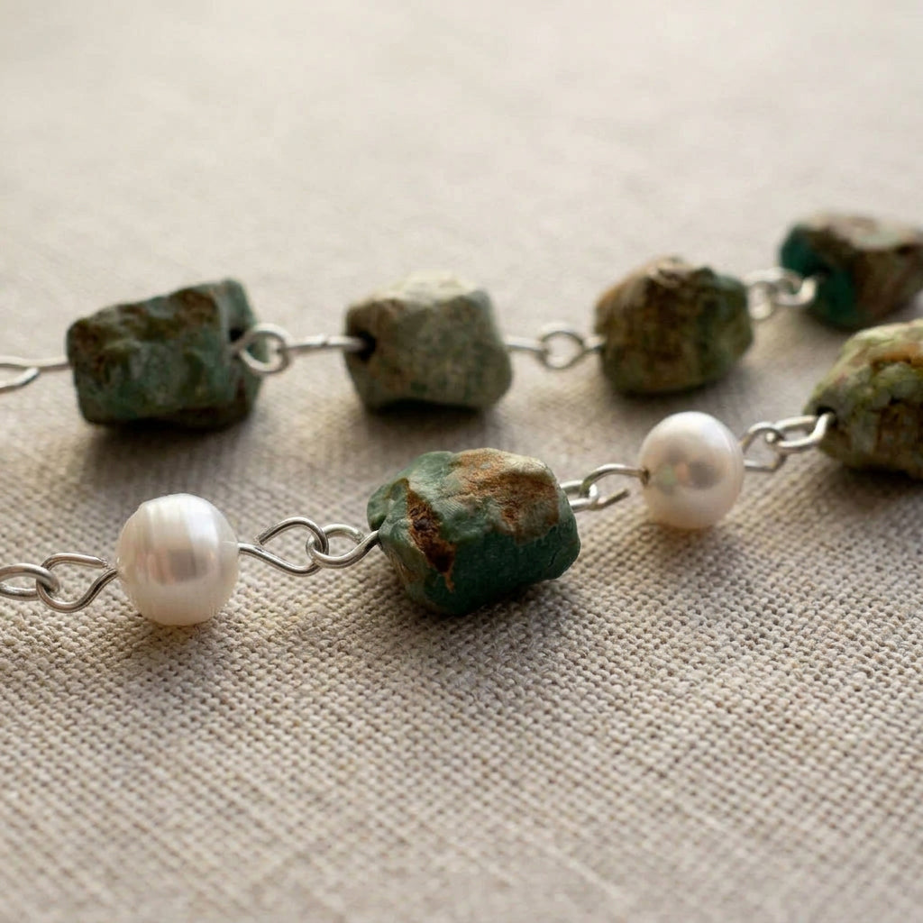 Close-up of raw green-blue Hubei turquoise stones with rough brown matrix and lustrous white baroque pearls, joined by handmade sterling silver wire loops on pale linen.