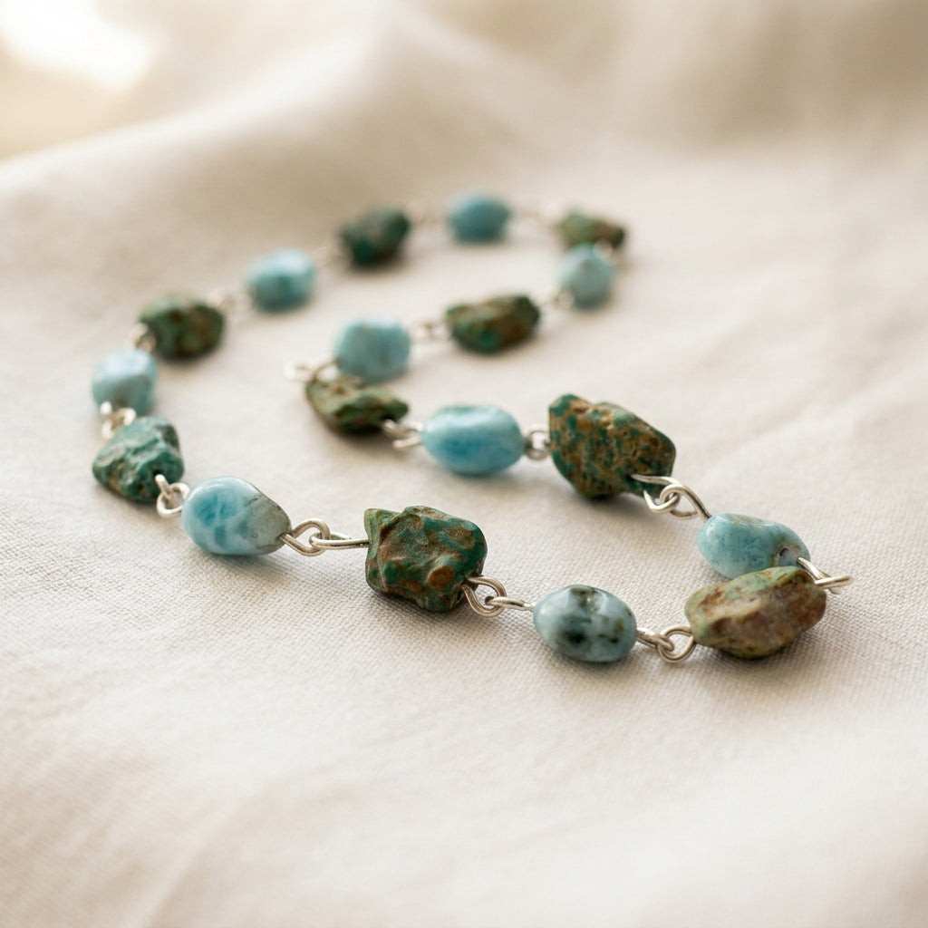 Sterling silver necklace arranged in loose curves on cream fabric, with raw green Hubei turquoise stones alternating with pale blue larimar beads.