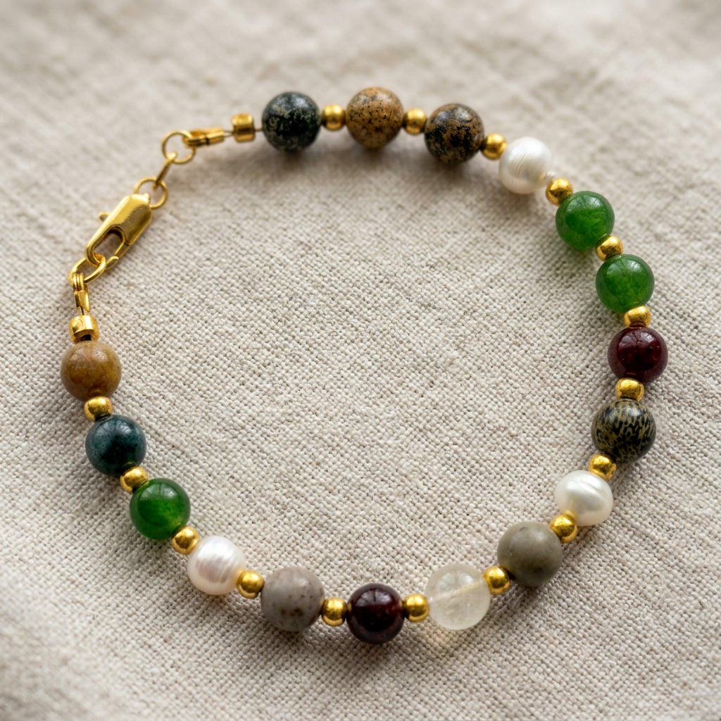 Beaded bracelet arranged in a circle on beige linen, with green, burgundy, patterned grey and translucent beads, white baroque pearls, gold-coloured spacers and a gold-filled lobster clasp.