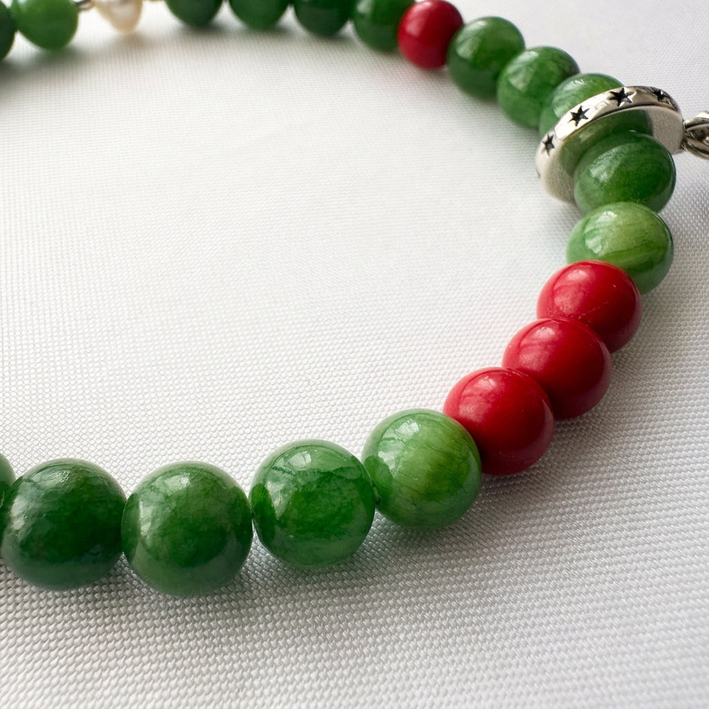 Close-up of three red coral beads among polished green jade beads, with a star-patterned charm holder on white fabric.