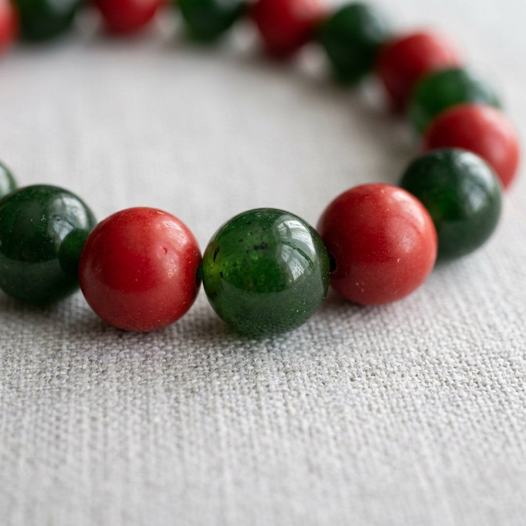 Close-up of alternating polished green jade and red coral beads on pale woven fabric.