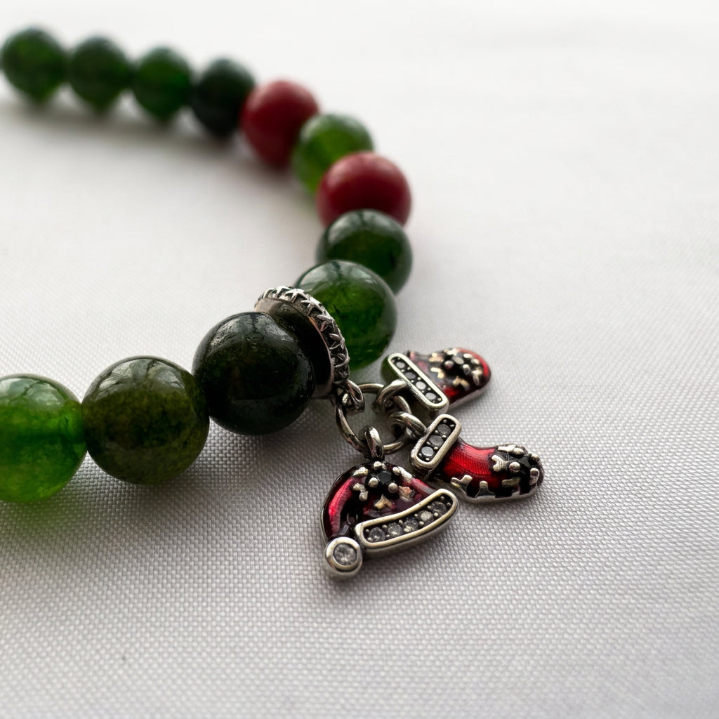 Close-up of red Santa hat and stocking charms with sparkling details on a green obsidian and red coral bracelet.