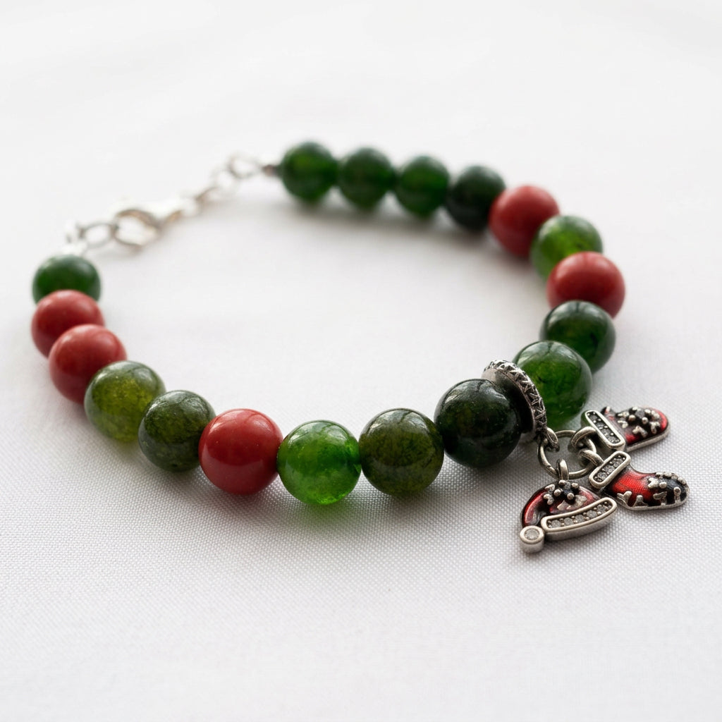 Green obsidian and red coral bracelet with red Santa hat and stocking charms, arranged in a circle on white fabric.