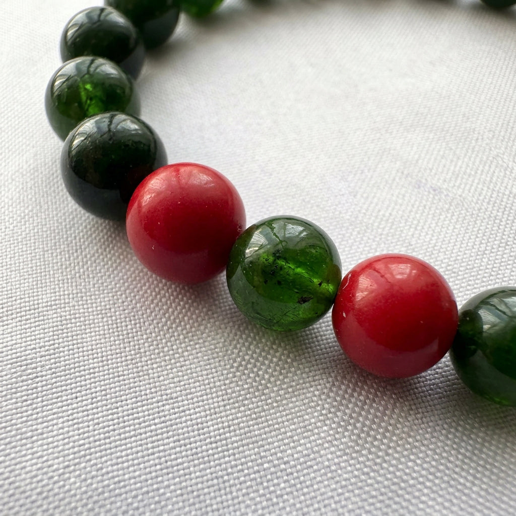 Close-up of a translucent green obsidian bead between two glossy red coral beads on white fabric.