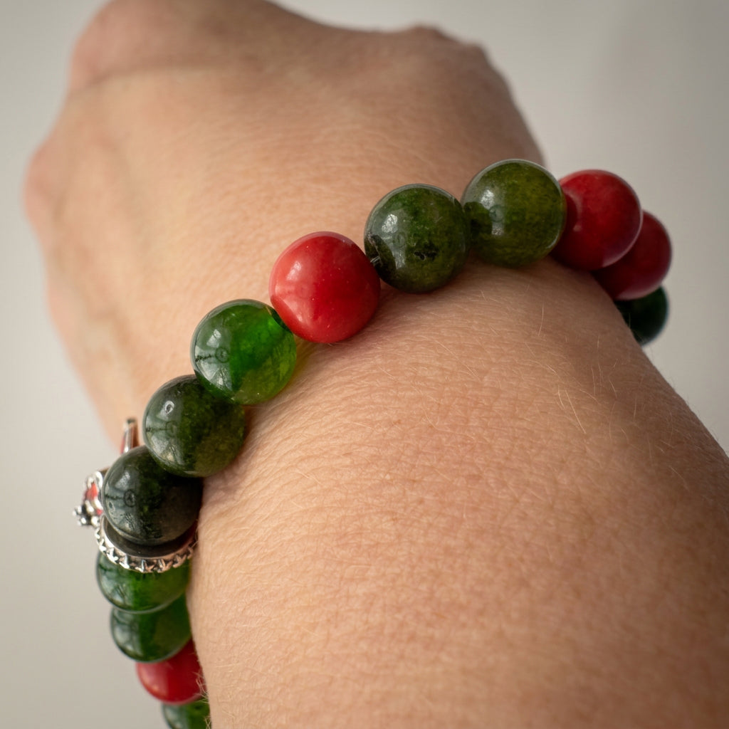 Green obsidian and red coral bracelet worn on a wrist, showing translucent green beads and glossy red accents.