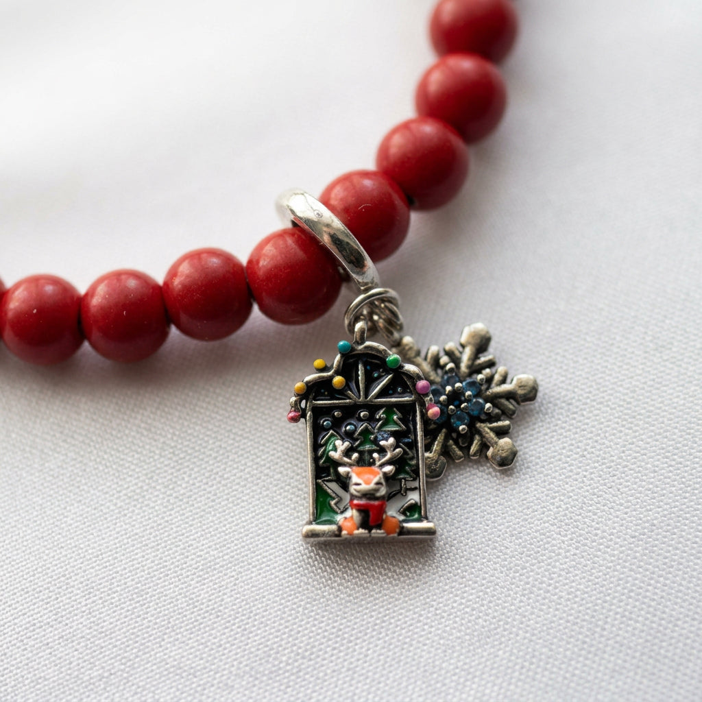 Close-up of reindeer Advent window and blue crystal snowflake charms on a red coral bracelet, resting on white fabric.