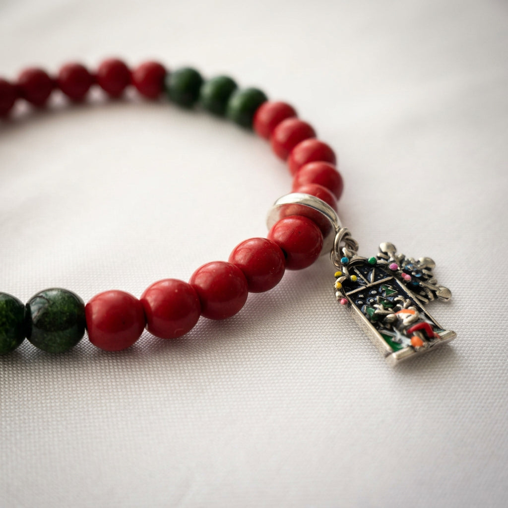 Angled view of a red coral and green sandstone bracelet with reindeer Advent window and snowflake charms on cream fabric.⠋