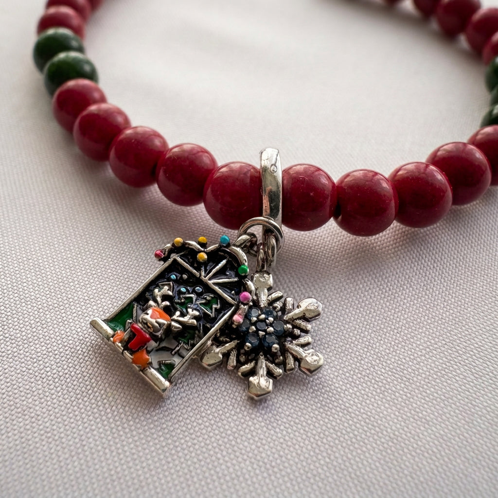 Close-up of reindeer Advent window and blue crystal snowflake charms beside glossy red coral beads on cream fabric.