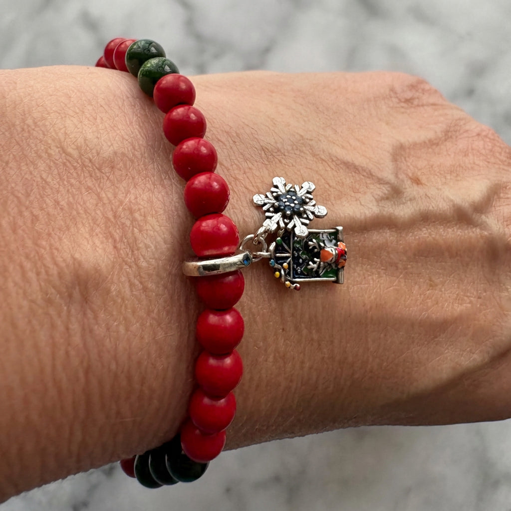 Red coral and green sandstone bracelet worn on a wrist, showing glossy red beads and sparkling dark green accents.