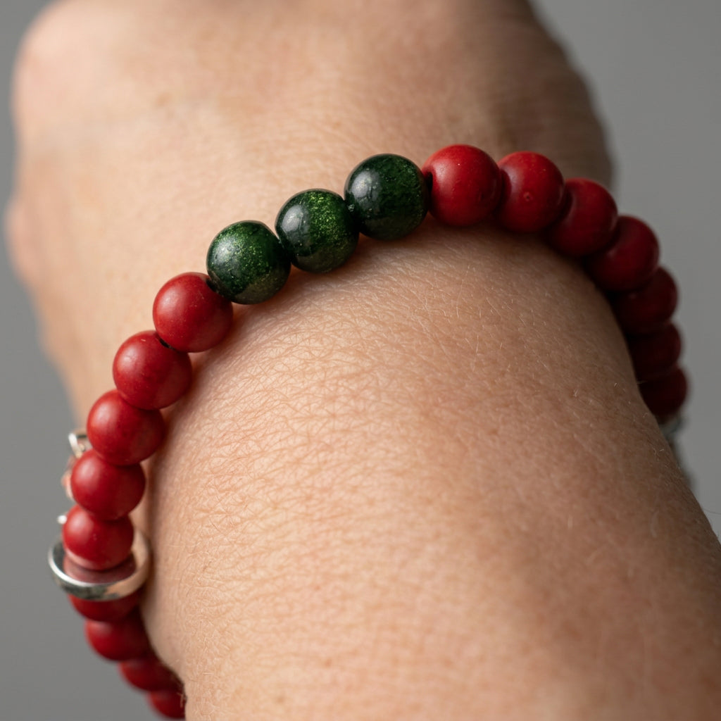 Red coral and green sandstone bracelet worn on a wrist, with a blue crystal snowflake and colourful reindeer Advent window charm.