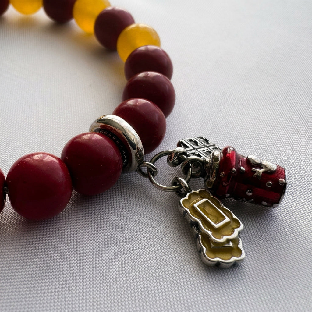 Close-up of red enamel bell, yellow sweet and silver-coloured gift charms beside red coral beads on white fabric.