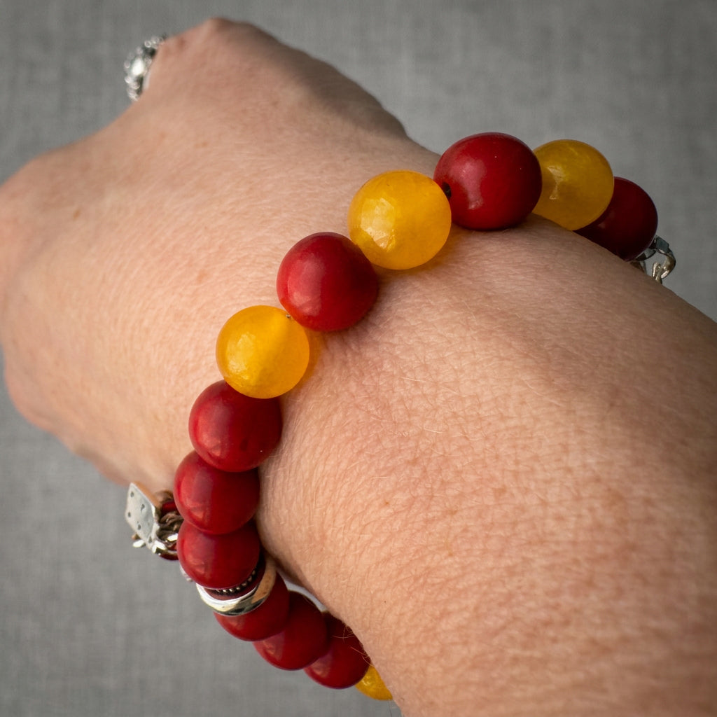 Red coral and yellow topaz bracelet worn on a wrist, showing glossy red beads interspersed with translucent yellow beads.