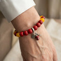Red coral bracelet with bright yellow topaz accents and dangling bell and gift charms, worn on the wrist beside a white silk shirt cuff.