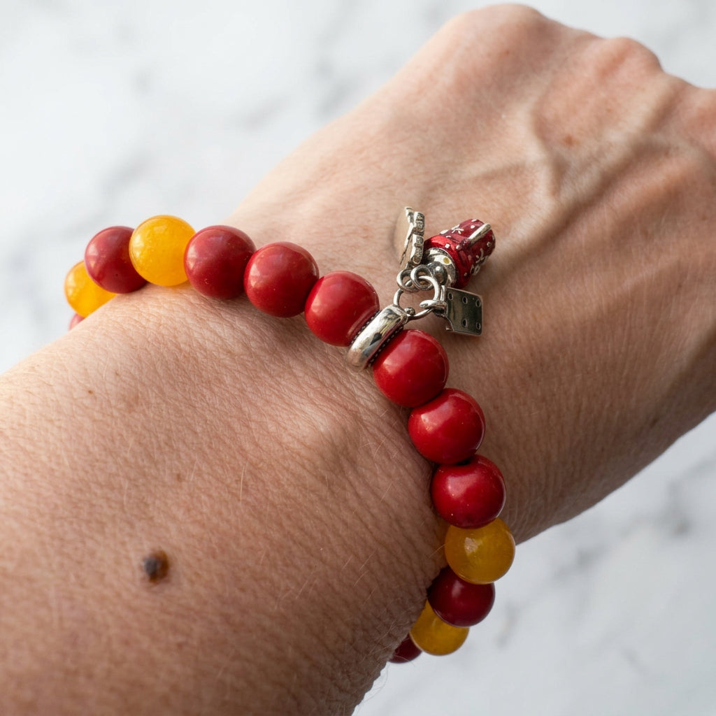 Angled wrist view of a red coral and yellow topaz bracelet with a red enamel bell and dangling Christmas charms.