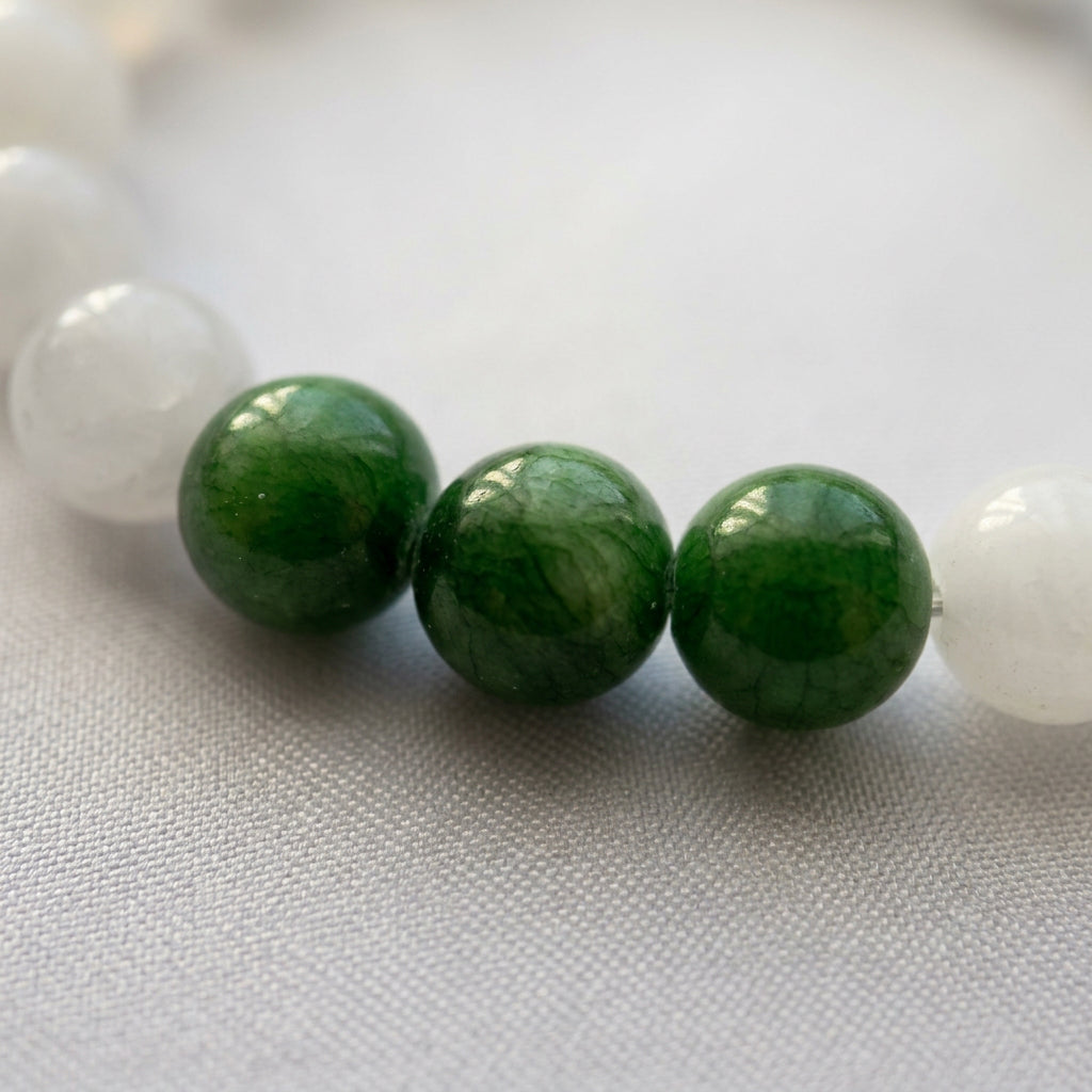 Close-up of three polished green jade beads between white jade beads on pale fabric.