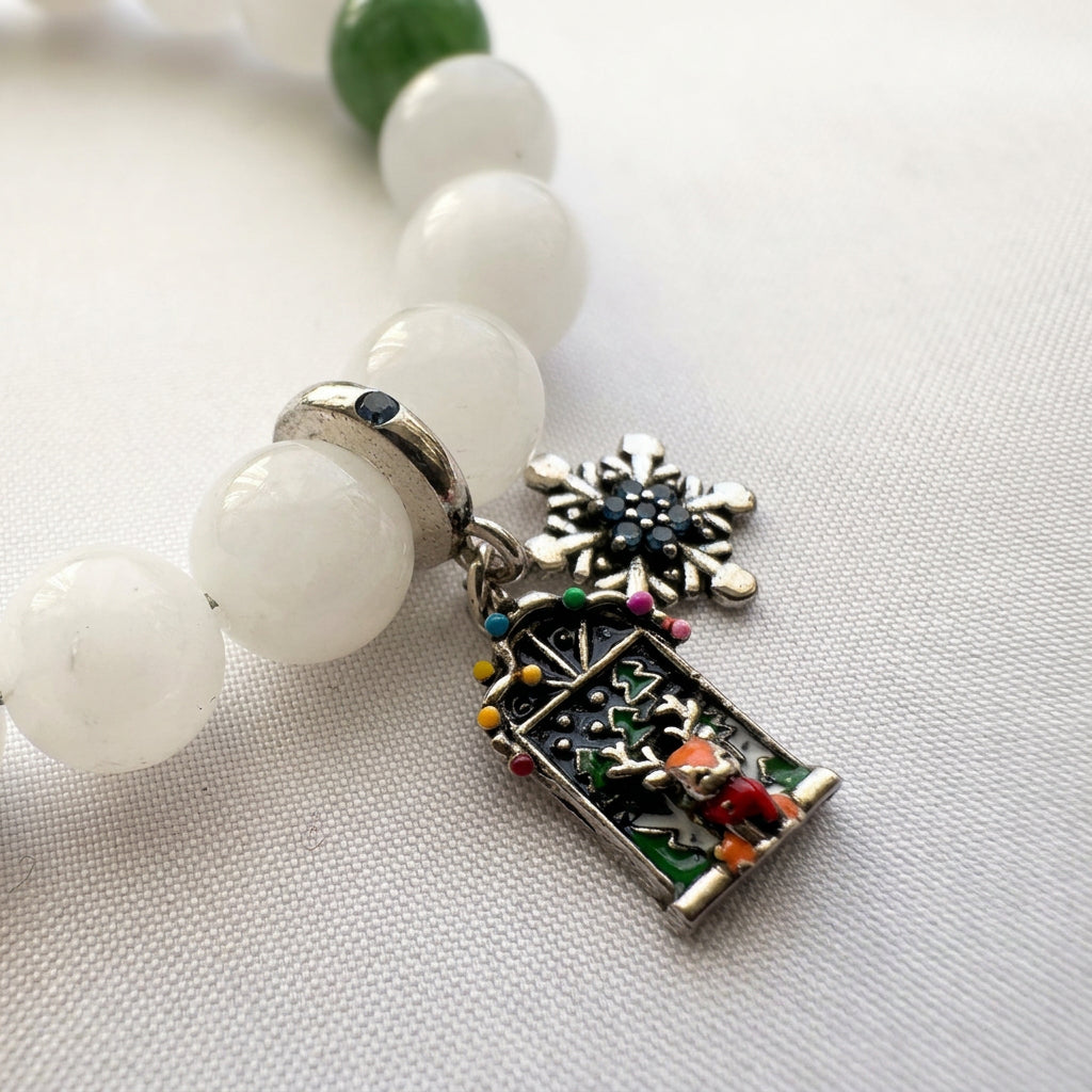 Close-up of reindeer Advent door and blue crystal snowflake charms beside white jade beads on pale fabric.⠋