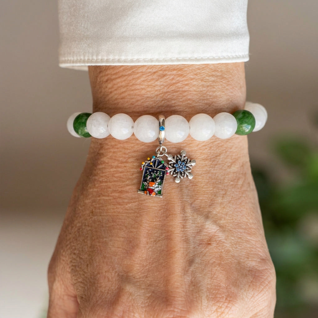 White jade bracelet with green jade accents, a blue-centred silver-coloured snowflake and colourful enamel advent door charm, worn on the wrist beside a white silk shirt cuff.