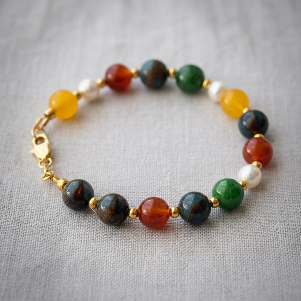 Beaded bracelet arranged in a circle on pale linen, with green jade, blue jasper, orange-red carnelian, yellow topaz, white baroque pearls and a gold-filled lobster clasp.