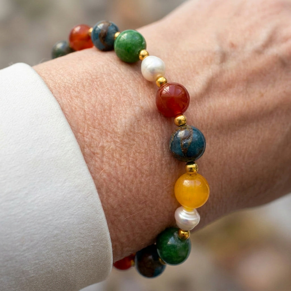 Green jade, mottled blue jasper, orange carnelian, yellow topaz and white pearl bracelet with gold-coloured spacers, worn on the wrist beside a white silk shirt cuff.