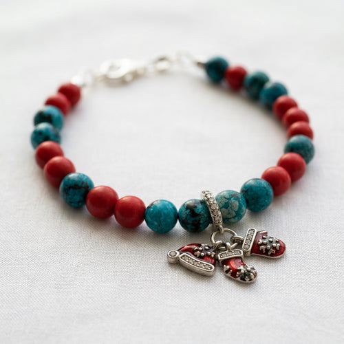 Blue agate and red coral bracelet with red enamel Santa hat and stocking charms, arranged in a circle on white fabric.