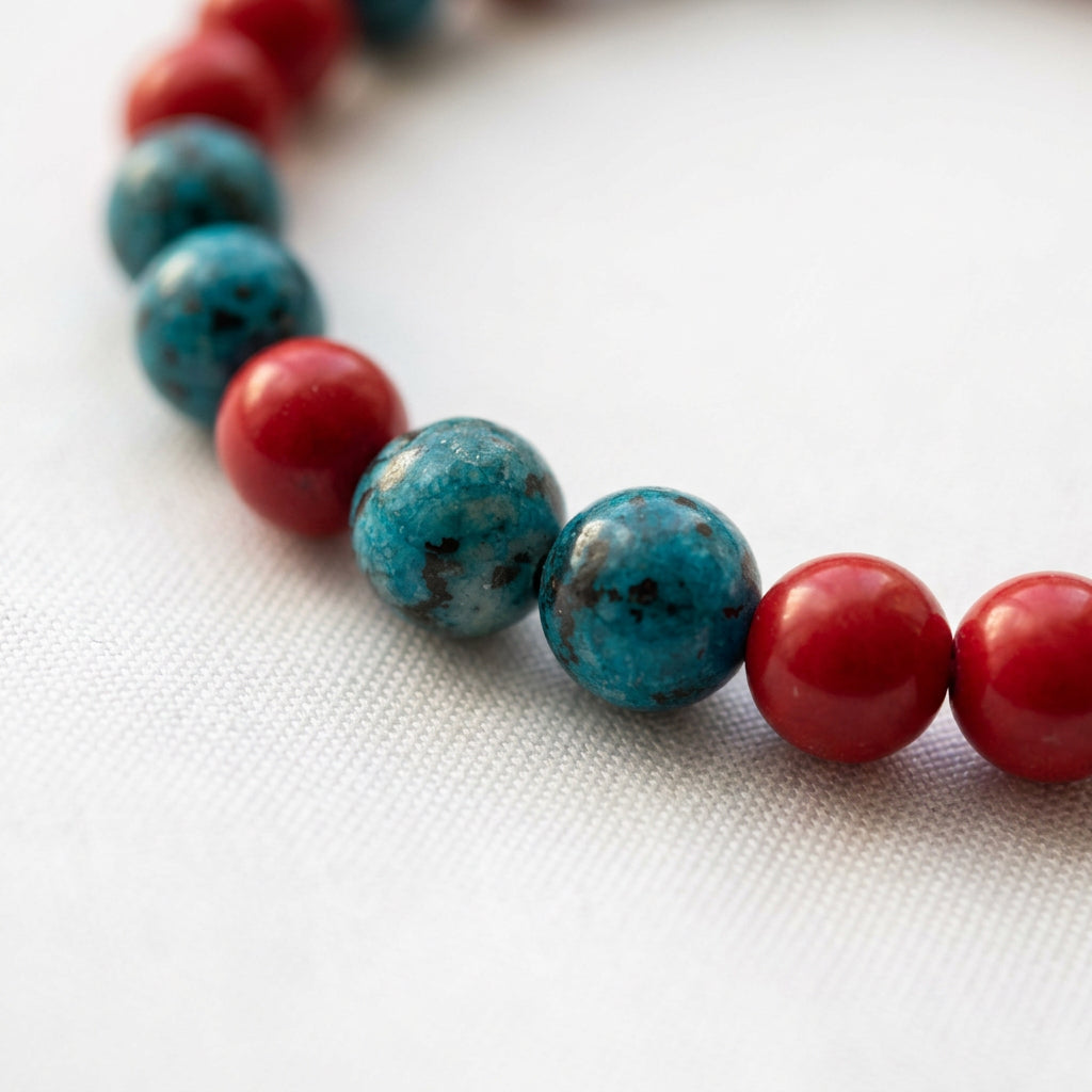 Close-up of two mottled blue agate beads beside glossy red coral beads on white fabric.