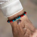 Faceted blue agate and red coral bracelet with dangling Santa hat and stocking charms, worn on the wrist beside a white silk shirt cuff.