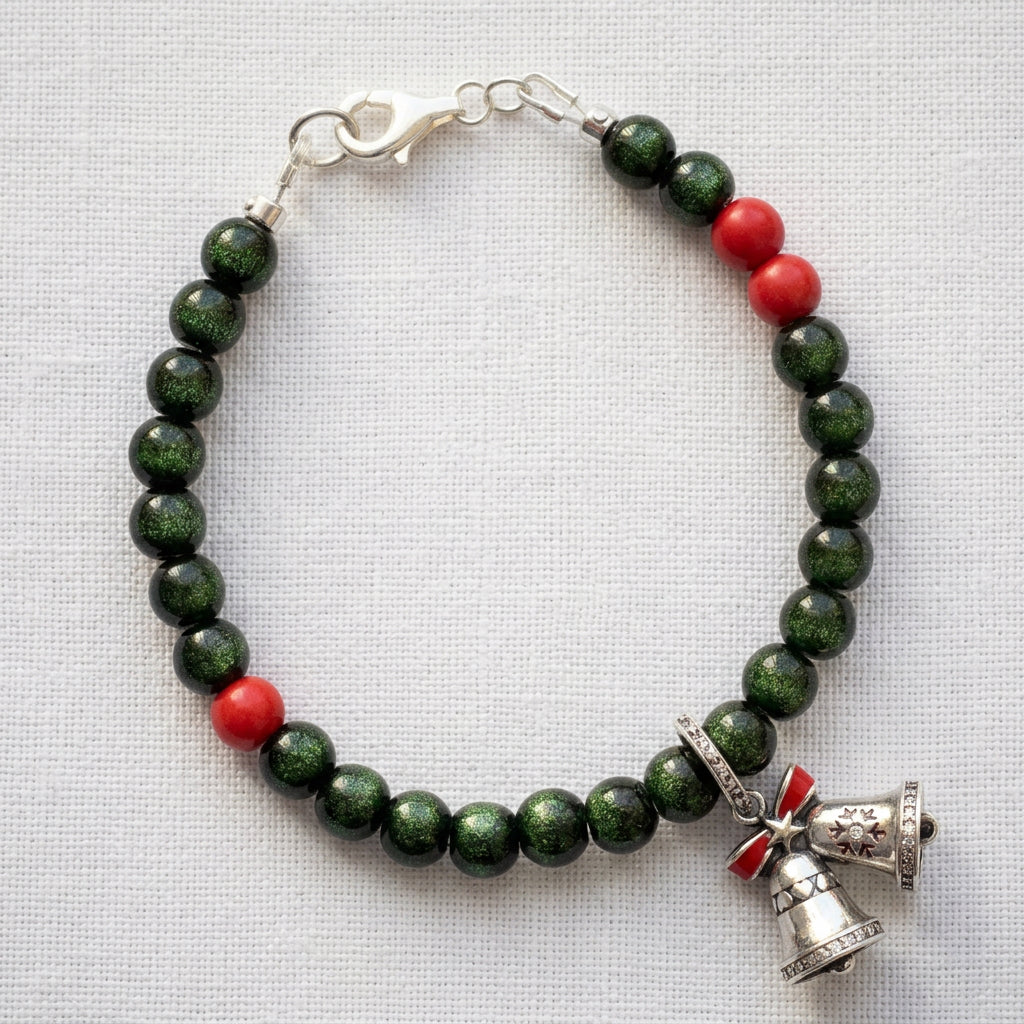 Green sandstone and red coral bracelet with twin bell charms and a red bow, arranged on white linen.