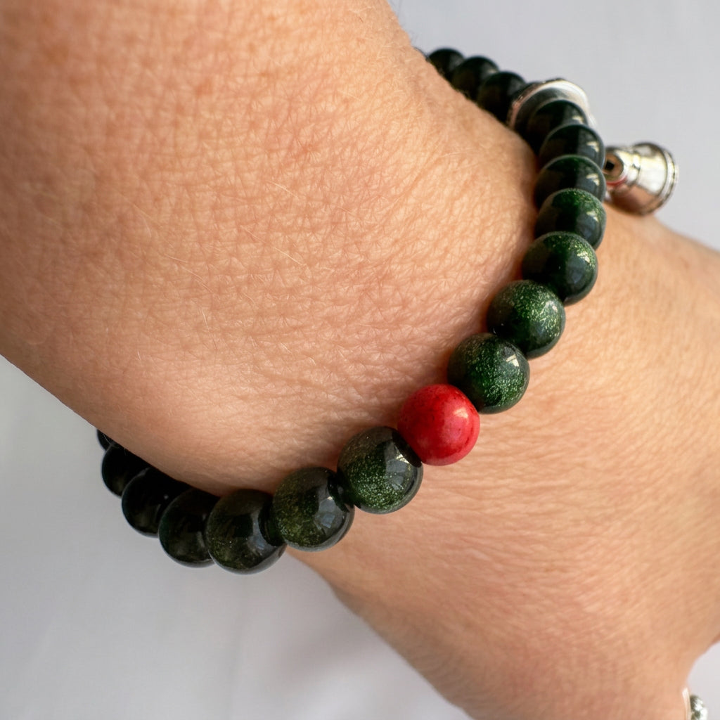 Green sandstone bracelet worn on a wrist, showing a red coral accent bead and bell charms hanging to one side.