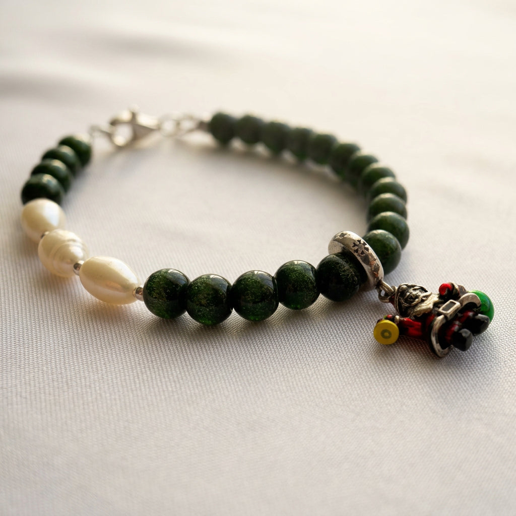 Green sandstone and white pearl bracelet with a colourful Santa charm, arranged on cream fabric.