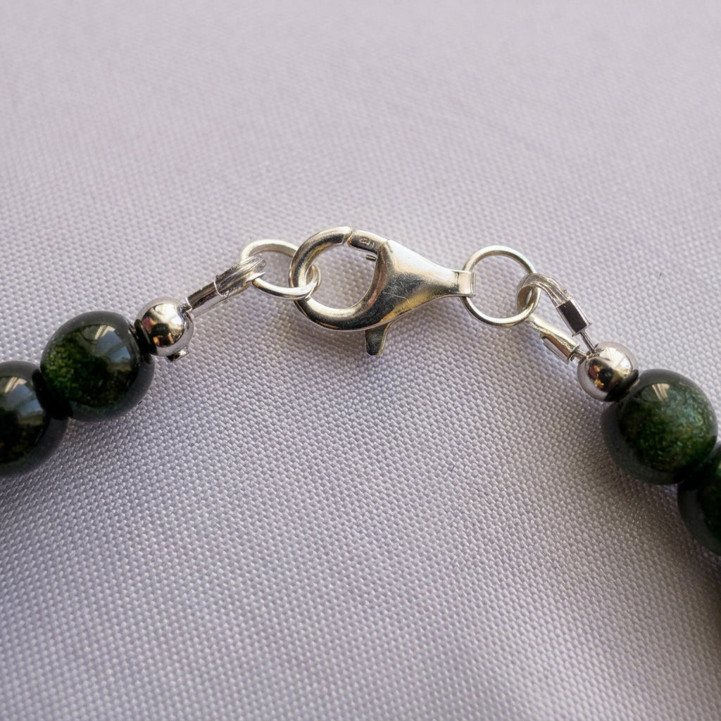 Close-up of the silver-coloured lobster clasp and connecting rings on a green sandstone bracelet, resting on pale fabric.