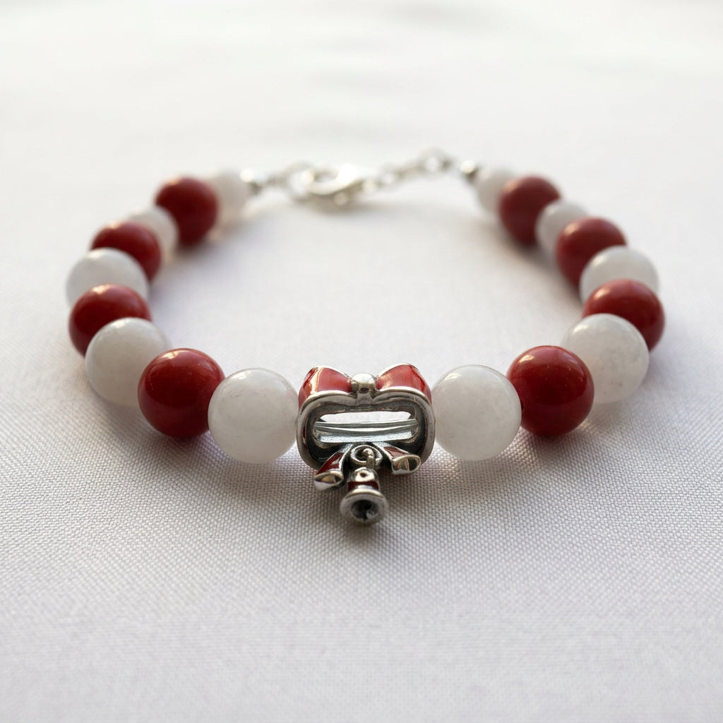 Rear view of the red bow charm and dangling bells between alternating red coral and white jade beads on white fabric.