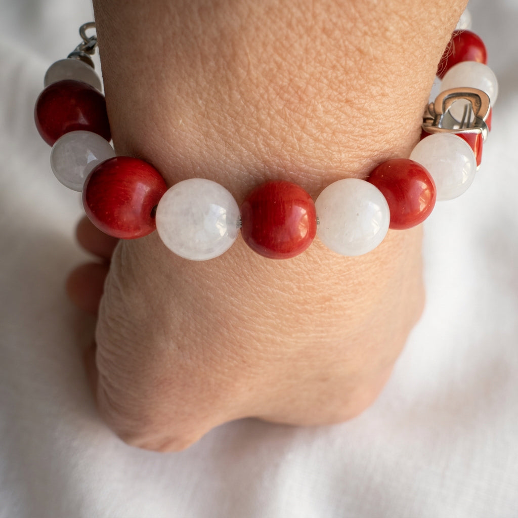 Close-up of alternating glossy red coral and white jade beads on a wrist, with the red bow charm visible to one side.