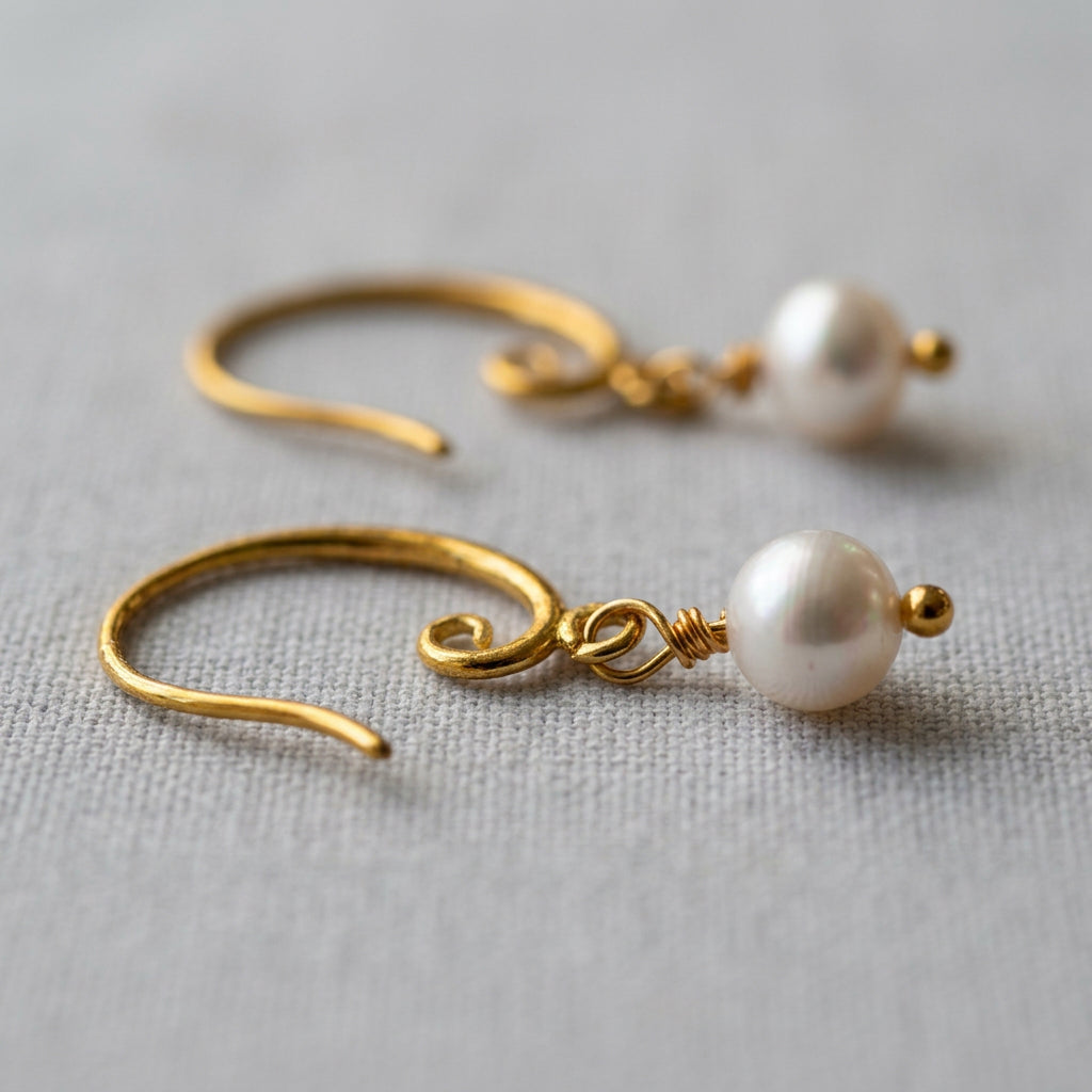 Close-up of white baroque pearl drop earrings on pale linen, showing gold-filled spiral hooks, wire-wrapped links and small gold bead tips.