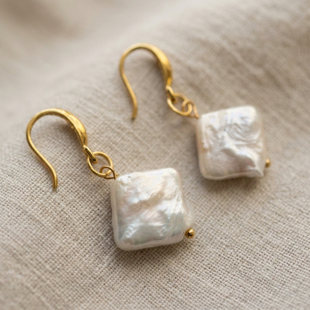 Side view of a white square baroque pearl drop earring worn on an ear, showing its slim profile, soft iridescent sheen and gold-filled hook.