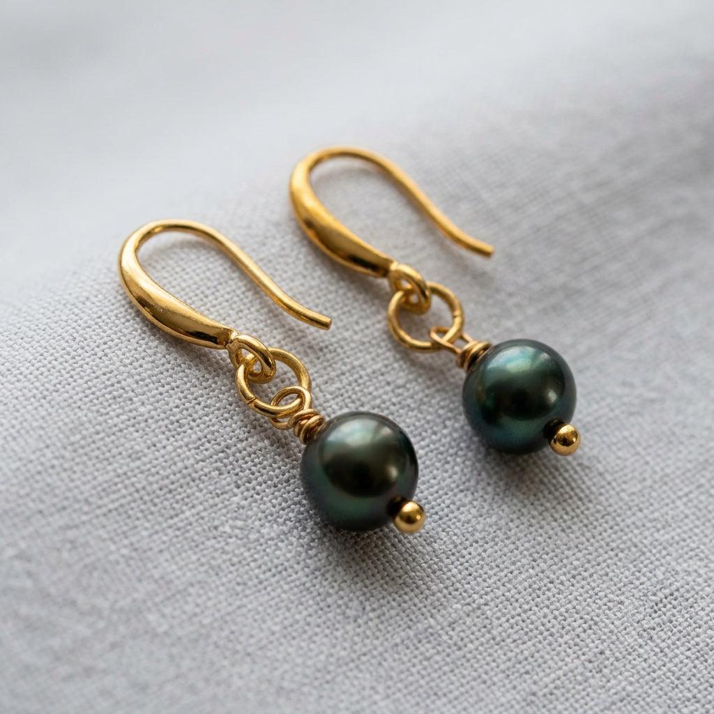 Pair of peacock baroque pearl drop earrings on pale linen, showing deep green iridescent pearls, gold-filled hooks and connecting rings.
