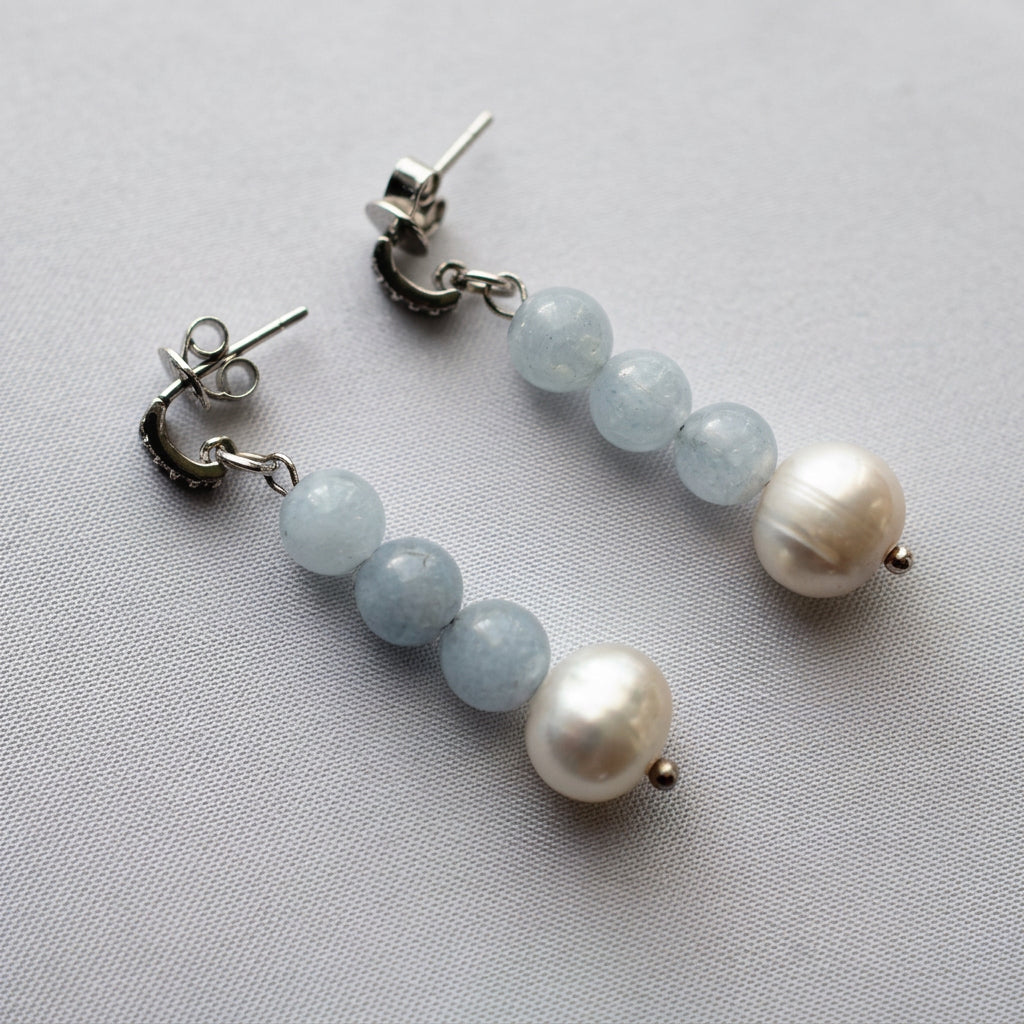 Pair of aquamarine and freshwater baroque pearl drop earrings on grey linen, each with three pale blue beads and a creamy white pearl, showing the sterling silver posts and butterfly backs.