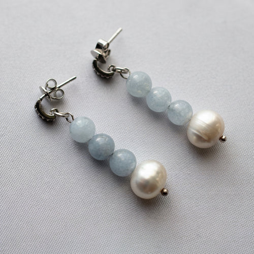 Pair of aquamarine and freshwater baroque pearl drop earrings on grey linen, each with three pale blue beads and a creamy white pearl, showing the sterling silver posts and butterfly backs.