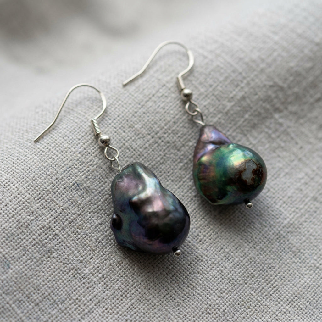 Dark blue keshi pearl earrings on light grey linen, showing their sculptural shapes and green, purple and gold iridescence.