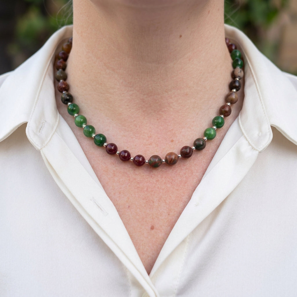 Green jade, red jasper and garnet necklace worn with an open-neck white shirt, showing groups of bright green beads, mottled earthy brown-red stones and deep burgundy garnets separated by small silver-coloured spacers.