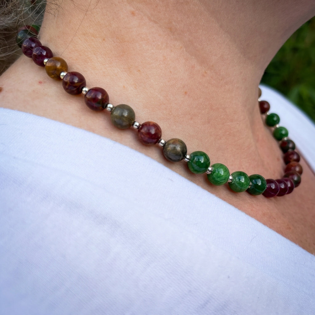 Side view of a green jade, red jasper and burgundy garnet necklace worn at the collarbone, with silver-coloured spacers between the beads.