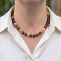 Blue jasper, carnelian, yellow topaz and white pearl necklace worn with an open-neck white shirt, showing mottled blue-green beads, rich orange-red stones, bright yellow accents and small gold-coloured spacers.⠋