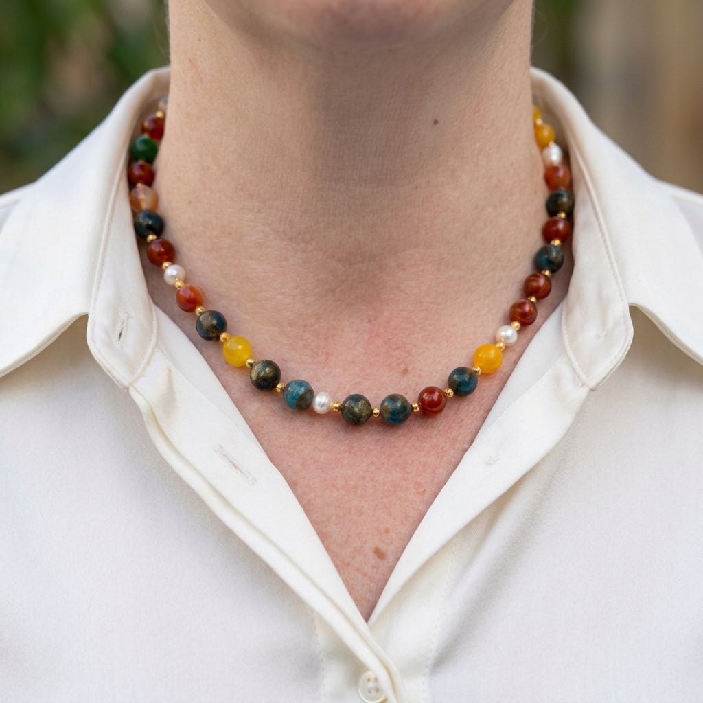 Blue jasper, carnelian, yellow topaz and white pearl necklace worn with an open-neck white shirt, showing mottled blue-green beads, rich orange-red stones, bright yellow accents and small gold-coloured spacers.⠋