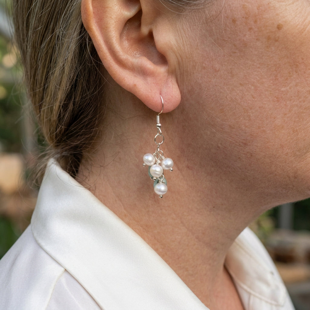 White baroque pearl and blue larimar cluster drop earrings on pale fabric, showing naturally varied stones, sterling silver wire-wrapped links and hook fittings.