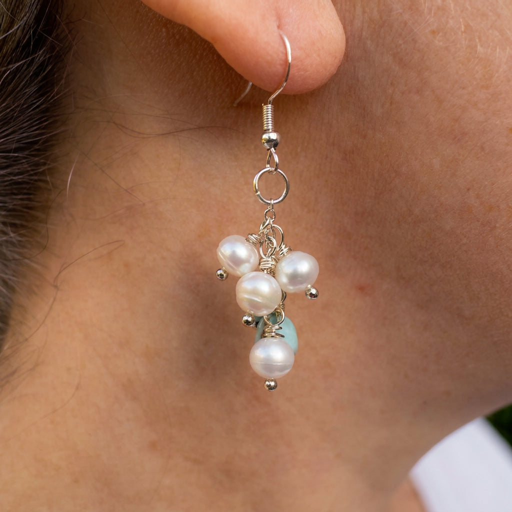 White baroque pearl and pale blue larimar cluster drop earring worn below the earlobe, showing dangling pearls, sterling silver links and a hook fitting.