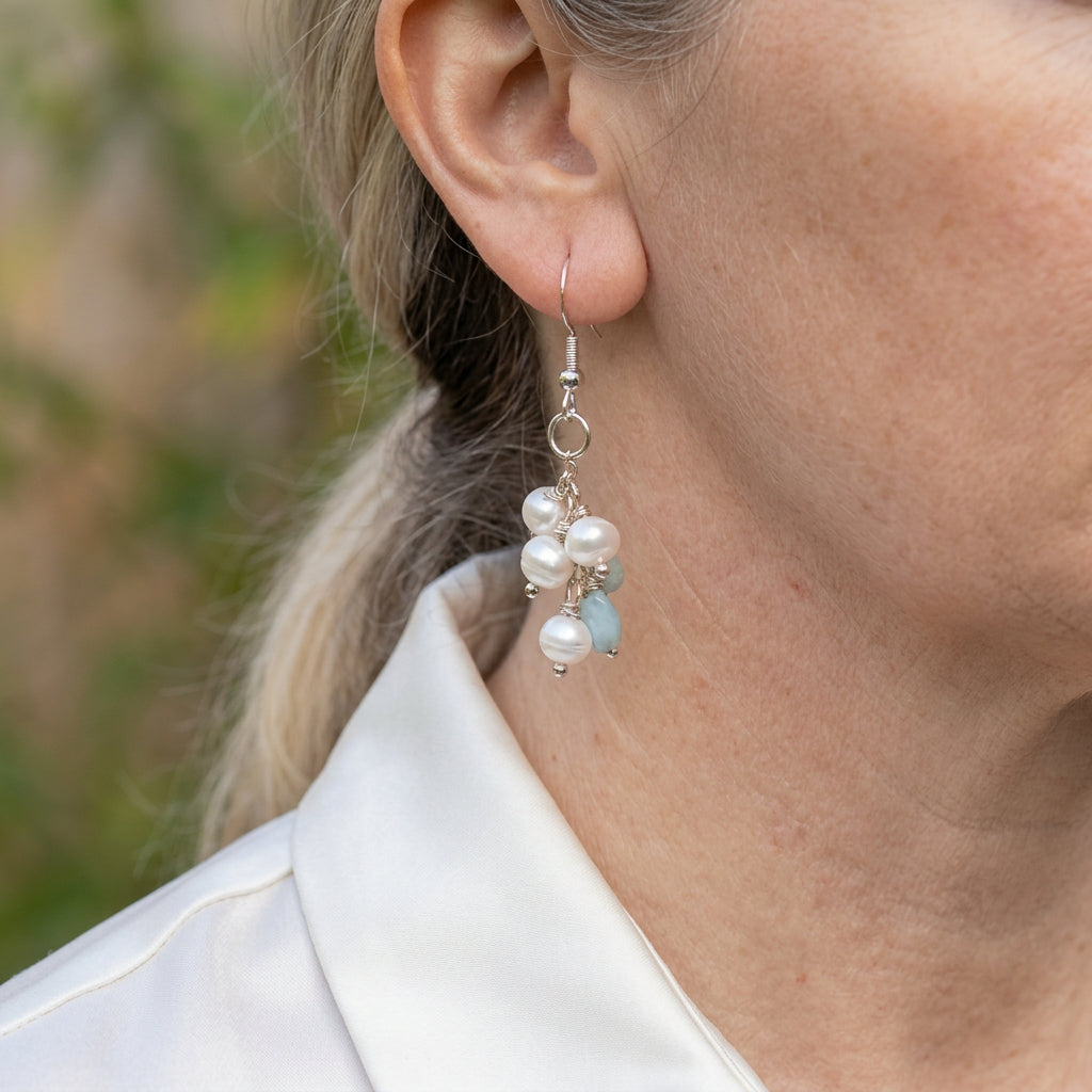 White baroque pearl and pale blue larimar cluster drop earring worn on an ear, with sterling silver wire-wrapped links and a hook fitting.