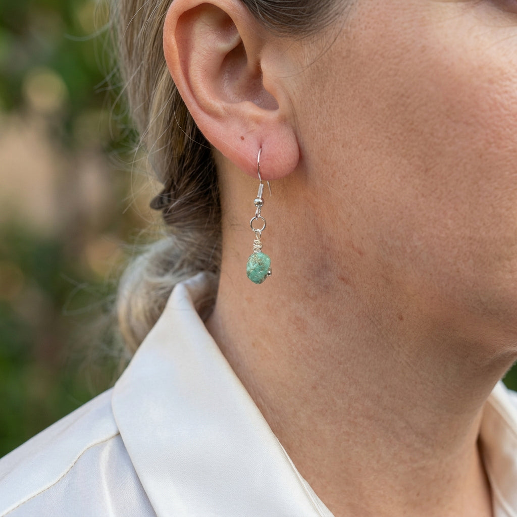 Raw blue-green Hubei turquoise drop earring on a sterling silver hook, shown worn above a white shirt collar, highlighting the stone’s irregular shape and natural surface texture.